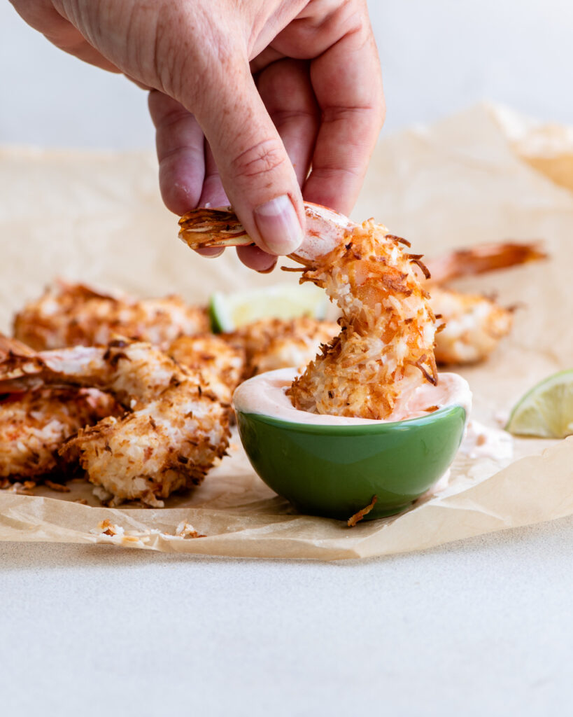 a hand dipping a piece of shrimp in a sweet spicy dip.