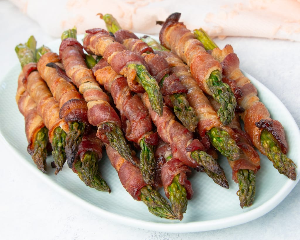 A recipe for keto bacon wrapped asparagus that can be served as a side dish, and adding a Swerve Brown "sugar" glaze makes these over-the-top delicious.